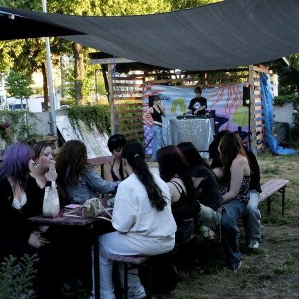 Zehn junge Menschen sitzen im Garten der Luise und hören dem DJ zu